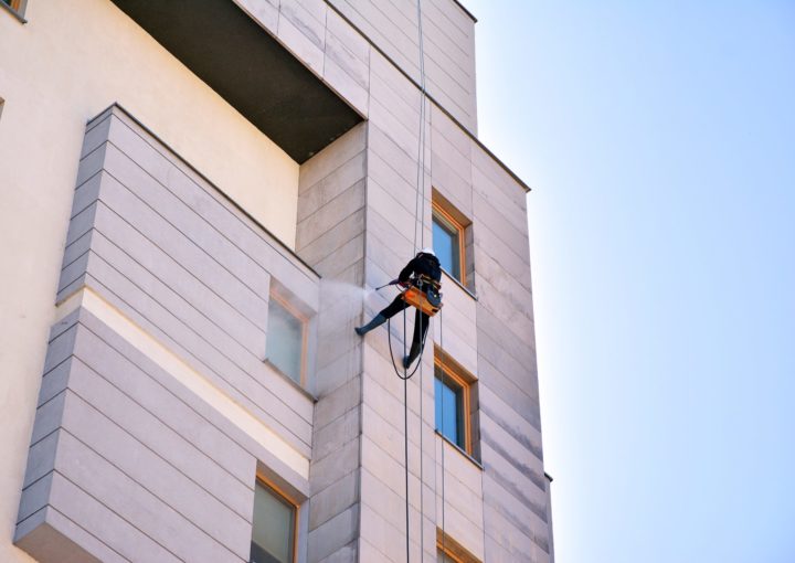 Un operario anclado verticalmente limpia la fachada ventilada cerámica tras su instalación